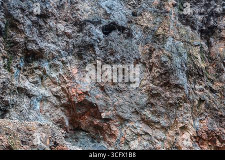 Trama dettagliata di una scogliera di roccia naturale che mostra strati di pietra con tonalità grigie, marroni e rossastre. Foto Stock