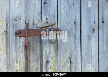 Dispositivo di chiusura in metallo su porta in legno grigio resistente agli agenti atmosferici. Legname naturale invecchiato nel tempo, mettendo in risalto texture, patina e artigianato rustico nordico nell'arcipite rurale Foto Stock