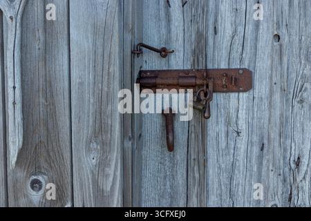 Dispositivo di chiusura in metallo su porta in legno grigio resistente agli agenti atmosferici. Legname naturale invecchiato nel tempo, mettendo in risalto texture, patina e artigianato rustico nordico nell'arcipite rurale Foto Stock