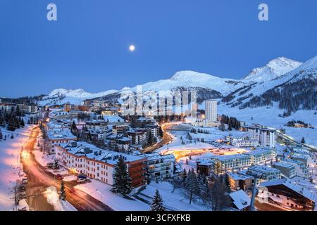 Veduta aerea della citta' delicatamente illuminata accoccolata tra cime innevate, con luci scintillanti contro il cielo blu crepuscolo, Sestriere, Piemonte, Italia. Foto Stock