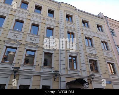 Una facciata storica beige con modanature bianche decorative e grandi finestre riflettenti si erge accanto ad un semplice edificio grigio. Questa foto acquisisce Foto Stock