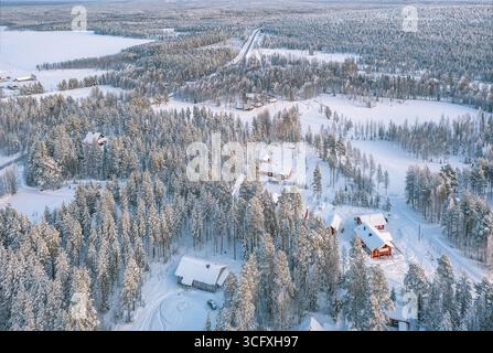 Vista aerea di sempreverdi carichi di neve e cabine rosse vivaci annidate in un paese delle meraviglie invernali, Rovaniemi, Lapponia, Finlandia. Foto Stock
