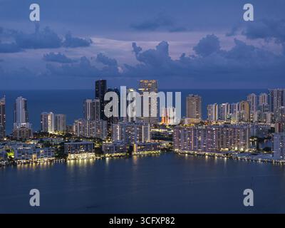Vista aerea dello skyline di Sunny Isles che si riflette nell'acqua di Dumfoundling Bay sotto il cielo crepuscolo, Aventura, Florida, Stati Uniti. Foto Stock