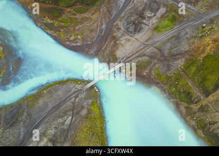 Vista aerea dei fiumi glaciali si incontrano sotto un ponte, le acque turchesi che attraversano l'aspro paesaggio degli altopiani, creando un incredibile contrasto di colori, altopiani e Islanda. Foto Stock