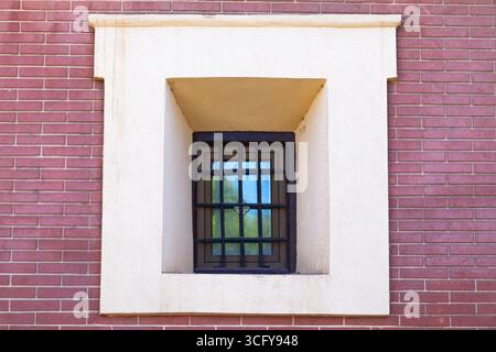 Una finestra con barrette arrugginite su di esso in un vecchio edificio in mattoni, primo piano. Foto Stock
