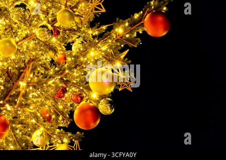 Rami dell'albero di Natale con luci calde, baule rosse e dorate e ornamenti a stelle su sfondo nero. Decorazioni invernali natalizie Foto Stock