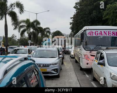 Questa immagine cattura il traffico intenso su una strada cittadina, con più auto, taxi e due grandi autobus, uno contrassegnato con "Shri Ganesh", con palme A. Foto Stock