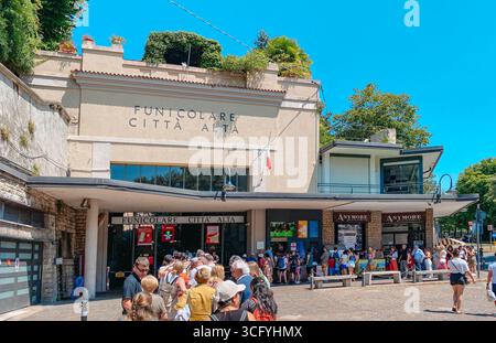 Bergamo, Italia - 22 giugno 2025: Una folla di persone in fila sotto il sole estivo fuori dalla stazione funicolare per Citta alta a Bergamo per cinghiali Foto Stock