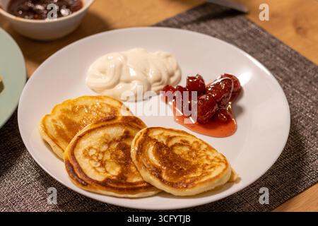 Pancake appena sfornati sul piatto di ceramica accanto alla marmellata di fragole e alla panna acida Foto Stock