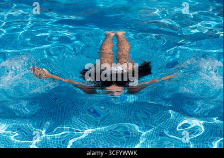 Giovane donna che nuota sott'acqua in una piscina blu con piastrelle a mosaico Foto Stock