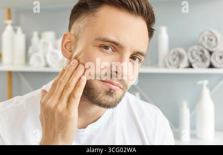 Giovane che spalma una crema idratante per l'idratazione della pelle durante la routine di cura della pelle al mattino Foto Stock