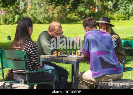 Gruppo di amici che giocano a scacchi all'aperto in un parco, divertendosi insieme in una giornata di sole Foto Stock