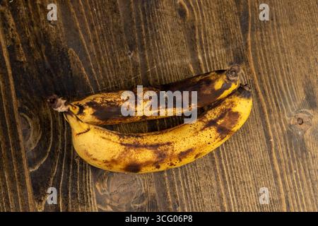 banana ultra matura annerita durante lo stoccaggio su una tavola di pino nero, banana marcificata annerita su un tavolo di legno Foto Stock