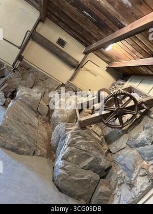 Ingranaggi di macchinari storici per l'estrazione mineraria incorporati nella roccia all'interno di una struttura conservata Foto Stock