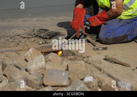Dettagli con un lavoratore che utilizza una torcia ossiacetilenica per tagliare i binari metallici del tram Foto Stock