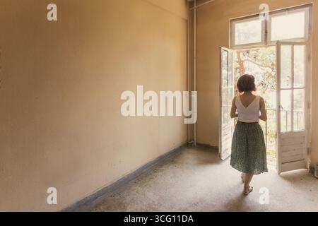 Donna che guarda fuori da una porta aperta in una stanza vuota Foto Stock