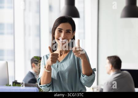 Donna d'affari in piedi in ufficio, che guarda la macchina fotografica e mostra il pollice in alto Foto Stock