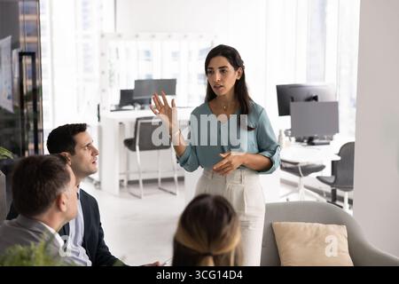 Una seria donna d'affari latina parla con fiducia davanti ai colleghi Foto Stock
