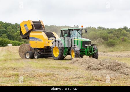 Imballaggio di fieno agricolo con imballatrice New Holland BR740 e trattore John Deere 6820 che produce balle di fieno circolari Foto Stock