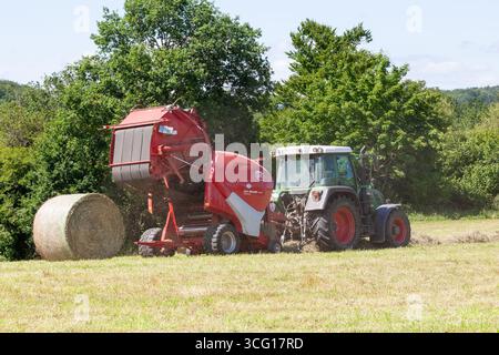 Agricoltore che utilizza un Lely Welger RP415 dietro un trattore Fendt per balle di fieno, balla circolare in uscita dall'imballatrice aperta che mostra le cinghie e i rulli Foto Stock