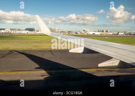 Vista dell'ala dell'aeroplano sulla pista con gli edifici dell'aeroporto sullo sfondo dell'aeroporto di Melbourne in Australia. Foto Stock