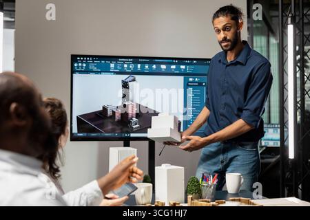 Ingegnere immobiliare maschile che presenta la progettazione di città intelligenti e la disposizione degli edifici, creando un piano generale con il suo team per la crescita delle infrastrutture residenziali e gli investimenti immobiliari moderni. Foto Stock