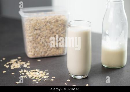 Un bicchiere di latte d'avena e farinata d'avena in una scatola sul tavolo da cucina grigio. Latte alternativo vegano e non lattiero-caseario Foto Stock