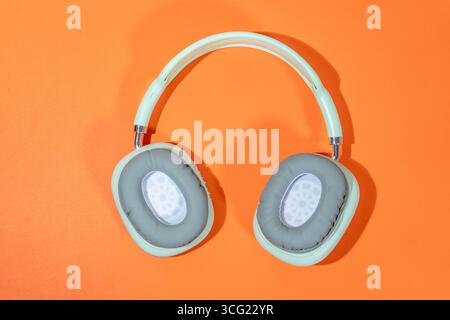 Eleganti cuffie wireless color verde chiaro su uno sfondo arancione brillante, che creano un contrasto sorprendente Foto Stock