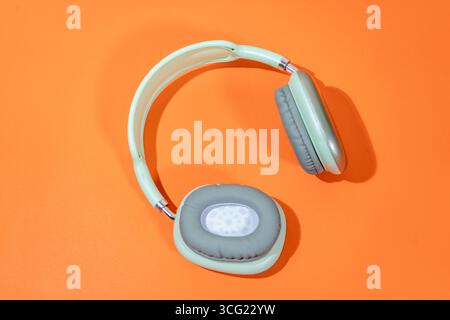 Eleganti cuffie wireless color verde chiaro su uno sfondo arancione brillante, che creano un contrasto sorprendente Foto Stock