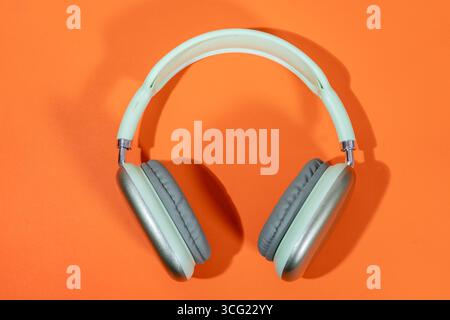 Eleganti cuffie wireless color verde chiaro su un vivace sfondo arancione, che rappresentano musica, tecnologia e divertimento audio Foto Stock