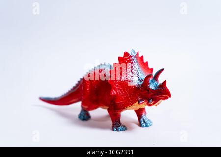 Giocattolo di dinosauro triceratops in plastica rossa su uno sfondo bianco senza cuciture, perfetto per progetti educativi o a tema preistorico Foto Stock