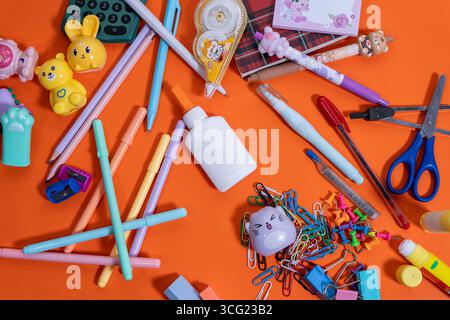 Forniture scolastiche colorate disposte su un vivace sfondo arancione per la stagione del ritorno a scuola Foto Stock