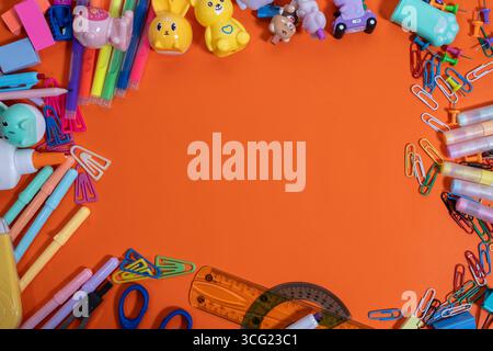 Disposizione vibrante delle forniture scolastiche per creare una cornice su uno sfondo arancione, perfetta per le promozioni Back to School Foto Stock