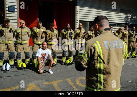 Londra, Regno Unito. 25 agosto 2025. I vigili del fuoco di base alla stazione dei vigili del fuoco di North Kensington hanno tenuto un minuto di silenzio in memoria dei 72 residenti morti nell'incendio della torre di Grenfell. Padre in lutto Ramiro Urbano, che ha tragicamente perso la figlia Jessica, si inginocchiò di fronte ai vigili del fuoco fuori dalla stazione, mostrando un tatuaggio dedicato a Jessie sul suo avambraccio. Credito: Fotografia dell'undicesima ora/Alamy Live News Foto Stock