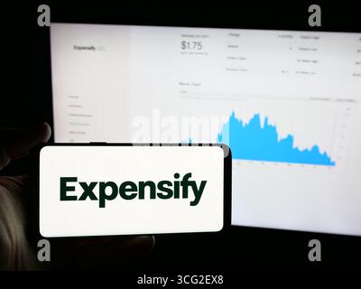 In questa immagine, una persona ha in mano uno smartphone con il logo della società di gestione delle spese Expensify Inc. Sullo schermo davanti al sito Web. Foto Stock