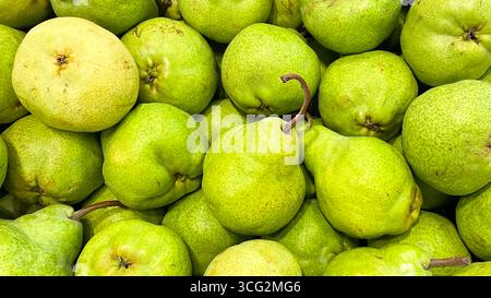 primo piano di una pila di pere verdi fresche, alcune con gambi marroni. Foto Stock