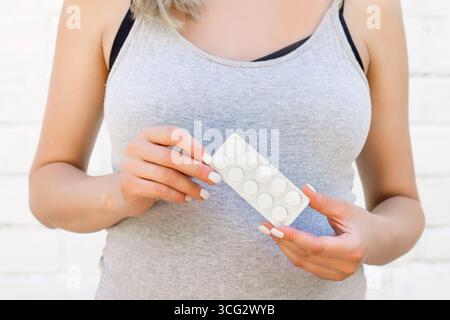 Donna incinta sullo sfondo di un muro di mattoni bianchi che tiene in mano una tavoletta. Salute della donna, concetto di ginecologia. Trattamento a freddo durante la pregna Foto Stock