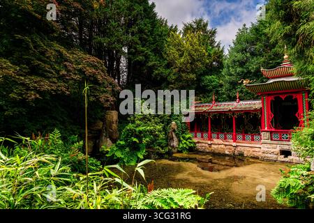 "Padiglione tradizionale in stile cinese circondato da vegetazione lussureggiante e laghetto riflettente in un tranquillo giardino botanico" Foto Stock