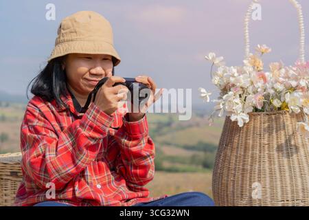 Una donna asiatica felice sta scattando foto con la sua macchina fotografica su un paesaggio di montagna. Concetto di viaggio e paesaggio Foto Stock