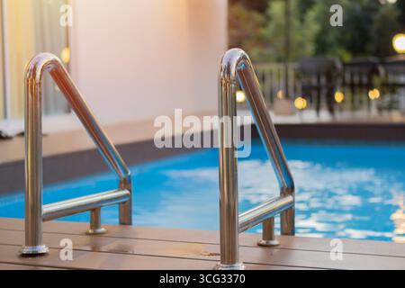 Primo piano di scale metalliche nella piscina di fronte a una casa in un resort. Scala per accedere alla piscina. Foto Stock