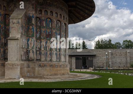 vista esterna di una chiesa ortodossa intemprata con affreschi religiosi colorati e dipinti sulle sue pareti esterne sotto un cielo nuvoloso Foto Stock