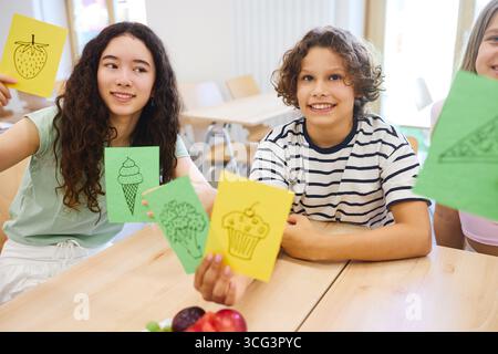 Un gruppo di studenti diversi seduti in una caffetteria che condivide illustrazioni gastronomiche e sorridono. Foto Stock