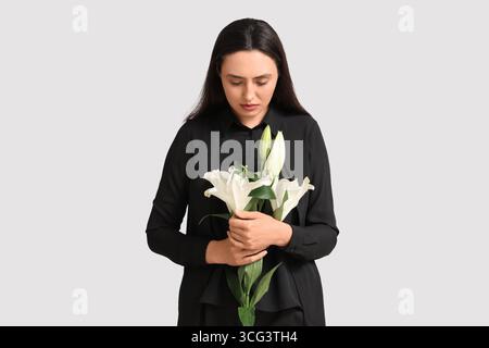 Giovane donna con bouquet funebre di fiori di giglio su sfondo bianco Foto Stock