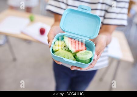 Un vivace cestino da pranzo contenente frutta e verdura fresche, tenuto all'interno di un'aula, che rappresenta le abitudini alimentari nutrienti e l'educazione abo Foto Stock