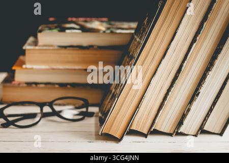 Libri chiusi con bicchieri su un tavolo di legno sullo sfondo di una serie di libri, tonalità vintage. Letteratura, concetto di apprendimento Foto Stock