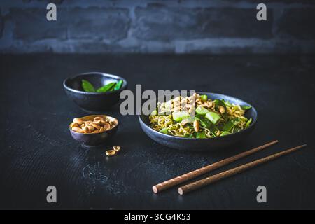 Tagliatelle asiatiche con cipolle primaverili e piselli di zucchero, condite con cetriolo e arachidi arrostite su sfondo nero Foto Stock