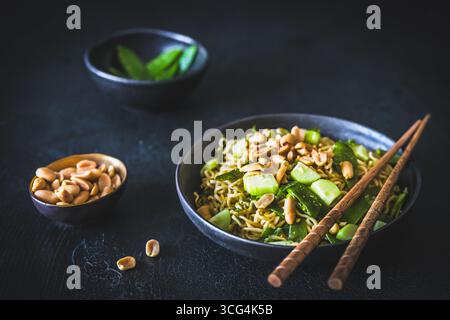 Tagliatelle asiatiche con cipolle primaverili e piselli di zucchero, condite con cetriolo e arachidi arrostite su sfondo nero Foto Stock