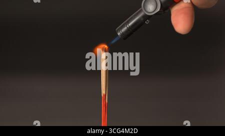 Un bastoncino di incenso con una piccola fiamma di torcia da vicino che tiene la torcia incenso rosso sfondo scuro calma spirituale meditazione rituale rilassamento Foto Stock