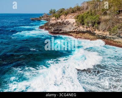 Costa rocciosa con potenti onde turchesi dell'oceano che si infrangono contro le scogliere sotto il cielo limpido. Foto Stock