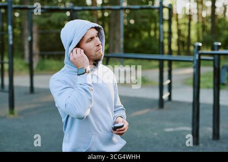 Uomo caucasico giovane adulto che regola gli auricolari mentre si fa esercizio all'aperto Foto Stock